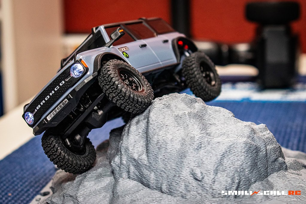 Small-scale RC off-road vehicle climbing over a rock obstacle.